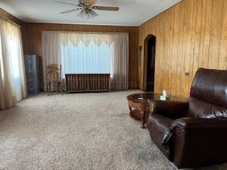 sitting room featuring wood walls, a wealth of natural light, ceiling fan, and carpet flooring