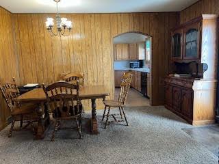 carpeted dining space featuring wooden walls and a notable chandelier