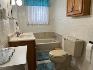 bathroom with toilet, vanity, a tub, and tile walls