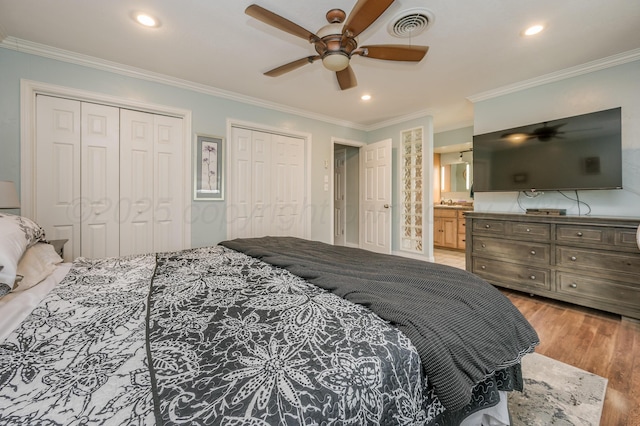 bedroom with crown molding, ceiling fan, connected bathroom, light hardwood / wood-style floors, and multiple closets