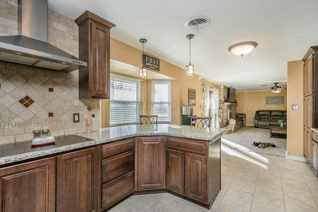 kitchen with light stone countertops, wall chimney range hood, kitchen peninsula, and decorative light fixtures
