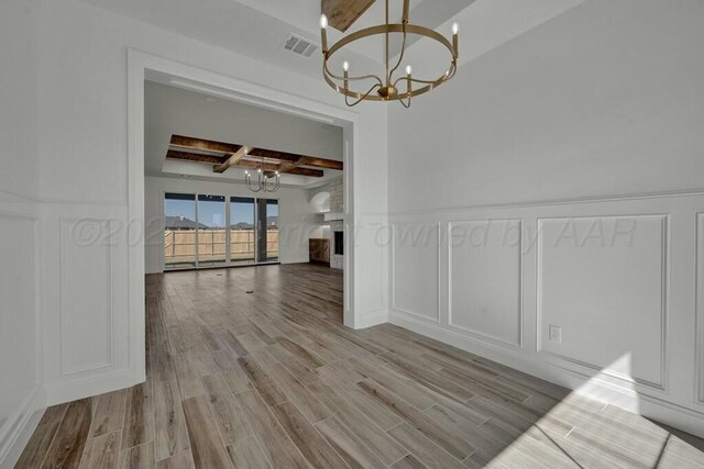 unfurnished dining area with a notable chandelier, visible vents, beamed ceiling, coffered ceiling, and a decorative wall