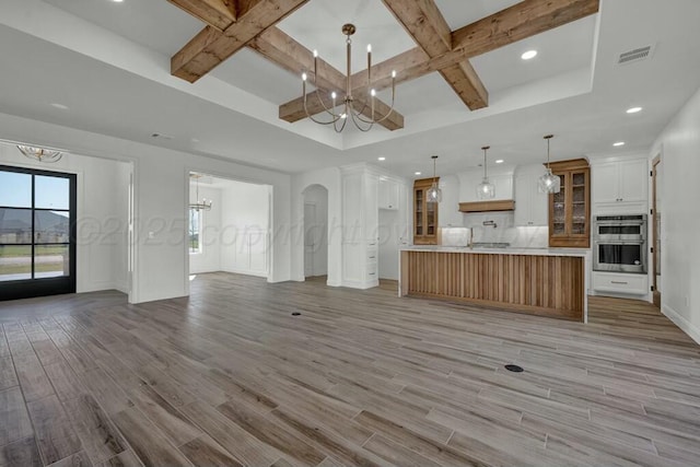 unfurnished living room with coffered ceiling, visible vents, light wood-type flooring, and a notable chandelier