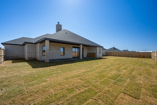 back of property featuring a fenced backyard, a lawn, roof with shingles, brick siding, and a chimney