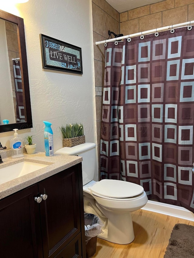 bathroom featuring a textured wall, toilet, vanity, wood finished floors, and a shower with curtain