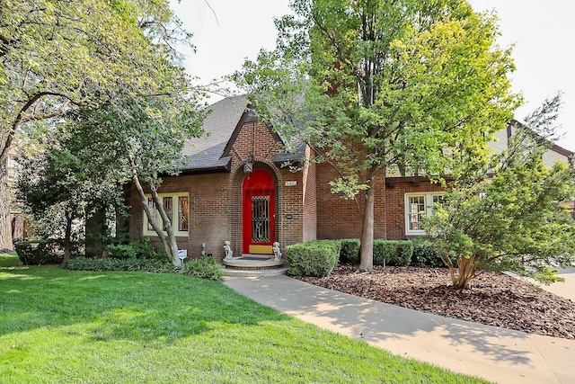 tudor house with brick siding, a front lawn, and a shingled roof