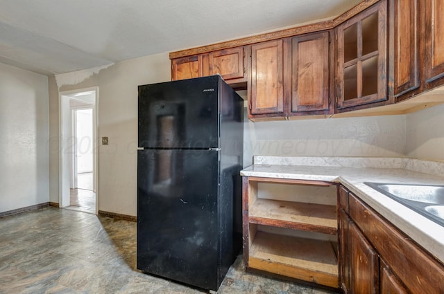 823 Ave N, Sunray, TX 79086 - kitchen with freestanding refrigerator, light countertops, glass insert cabinets, brown cabinets, and baseboards