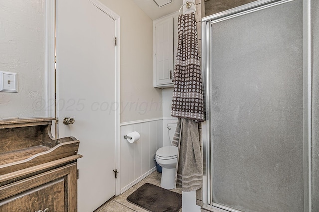 bathroom featuring wainscoting, toilet, tile patterned floors, and a shower stall