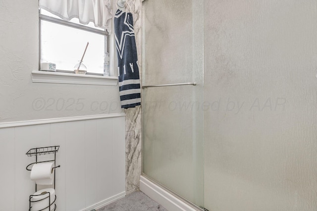 bathroom with a shower stall and a wainscoted wall