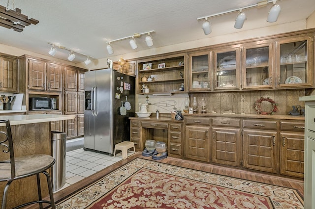 kitchen featuring light countertops, stainless steel fridge, light tile patterned floors, black microwave, and glass insert cabinets