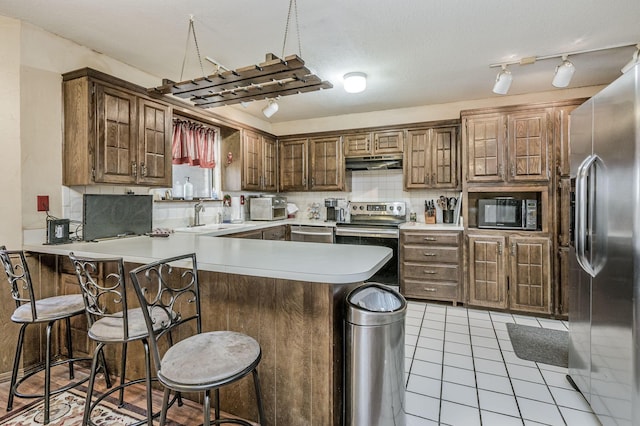 kitchen featuring light tile patterned flooring, a sink, appliances with stainless steel finishes, a peninsula, and under cabinet range hood