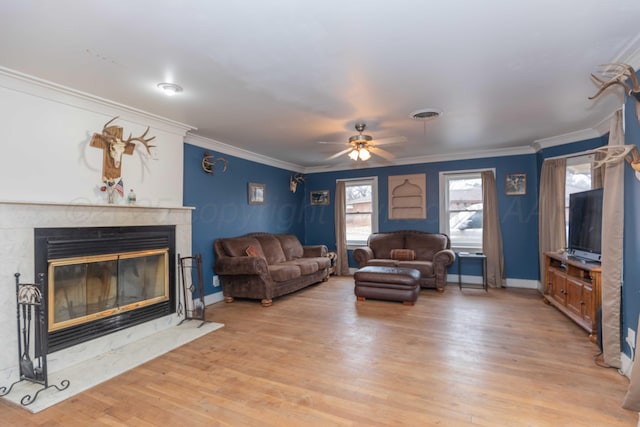 living room featuring ceiling fan, ornamental molding, a premium fireplace, and light hardwood / wood-style flooring