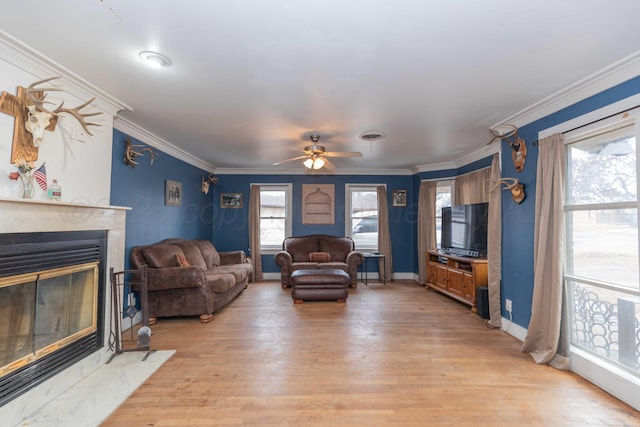 living room with ceiling fan, ornamental molding, a premium fireplace, and light hardwood / wood-style flooring