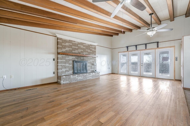 unfurnished living room featuring hardwood / wood-style flooring, vaulted ceiling with beams, a fireplace, and french doors