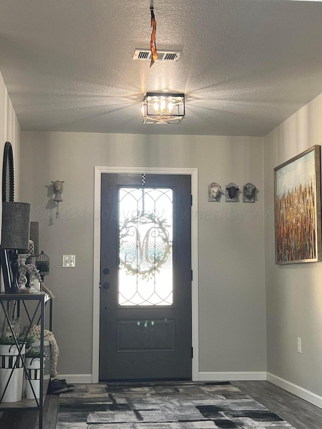 entryway featuring dark hardwood / wood-style flooring, an inviting chandelier, and a textured ceiling