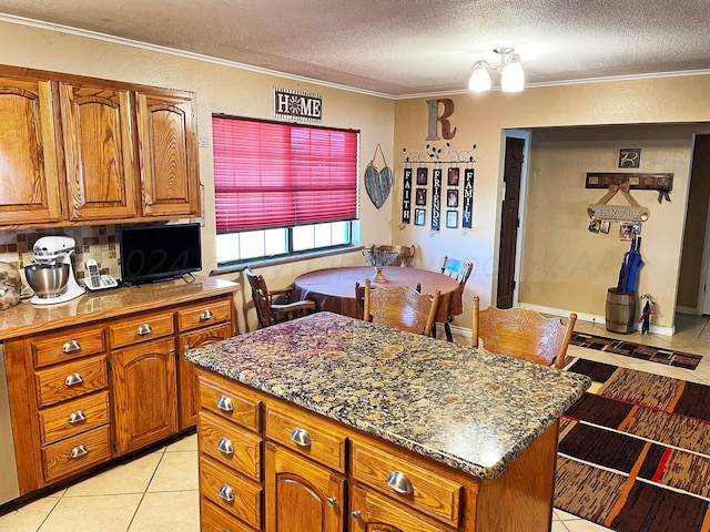 kitchen featuring crown molding, light tile patterned floors, a center island, and dark stone countertops