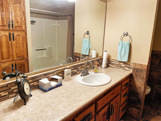 bathroom featuring a shower, vanity, toilet, and tasteful backsplash