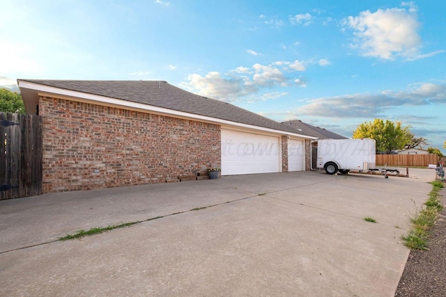 view of home's exterior with brick siding, a shingled roof, concrete driveway, and fence