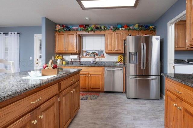 kitchen featuring a sink, brown cabinets, stainless steel appliances, and dark stone countertops