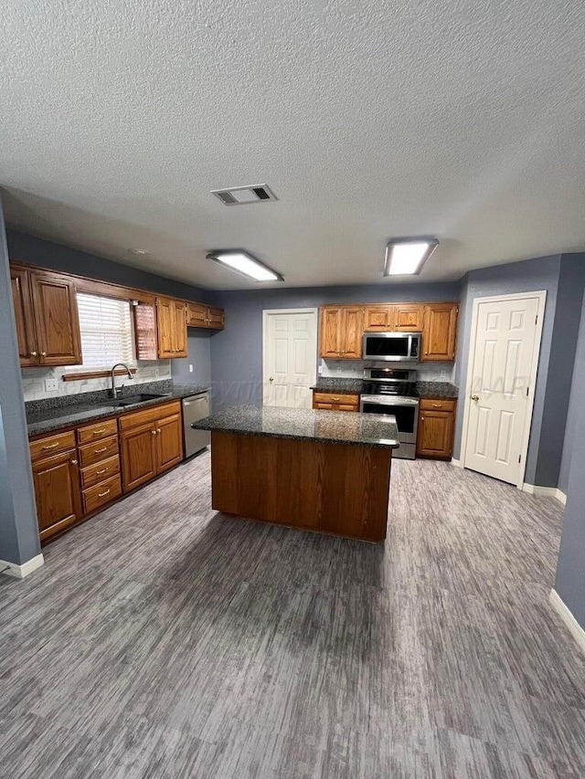 kitchen with visible vents, a sink, a kitchen island, stainless steel appliances, and brown cabinetry