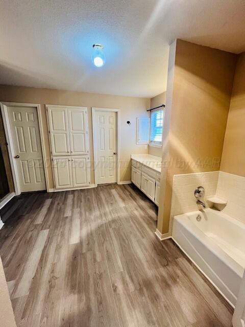 bathroom with vanity, wood finished floors, baseboards, a textured ceiling, and a garden tub