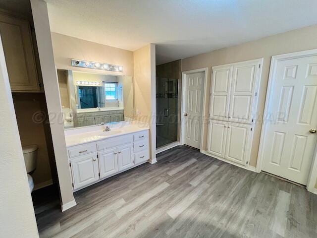 bathroom with vanity, wood finished floors, baseboards, a stall shower, and toilet