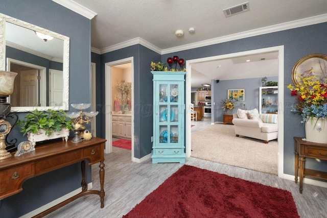 interior space with wood finished floors, visible vents, ensuite bath, ornamental molding, and a textured ceiling