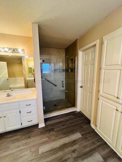 full bath featuring vanity, wood finished floors, a shower stall, and a textured ceiling