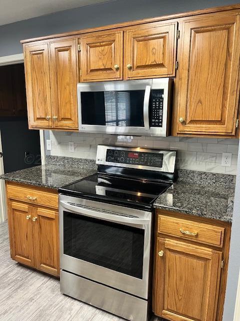 kitchen featuring brown cabinetry, backsplash, appliances with stainless steel finishes, and dark stone countertops