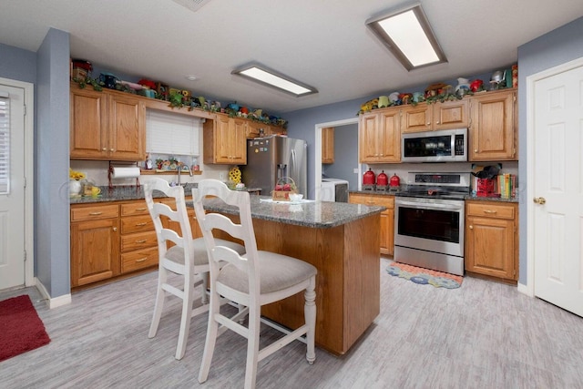 kitchen featuring washing machine and clothes dryer, a center island, a kitchen bar, light wood-style flooring, and stainless steel appliances