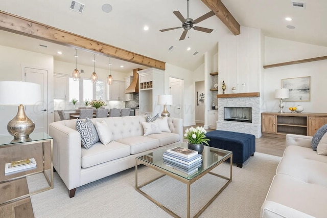 living area featuring a ceiling fan, a fireplace, visible vents, and beamed ceiling