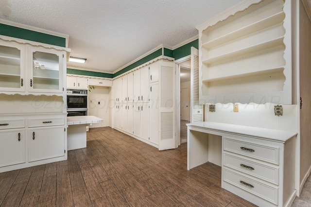 kitchen featuring crown molding, white cabinetry, a textured ceiling, dark hardwood / wood-style flooring, and black double oven