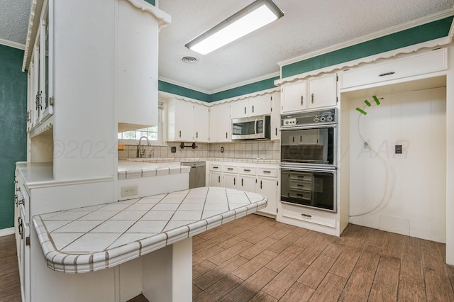 kitchen with stainless steel appliances, a textured ceiling, white cabinets, tile counters, and dark hardwood / wood-style flooring