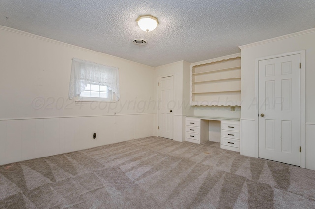 unfurnished bedroom with carpet flooring, a textured ceiling, and built in desk