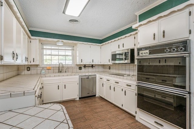 kitchen with white cabinetry, black appliances, tile countertops, and crown molding