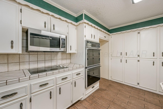 kitchen with white cabinets, tile counters, black double oven, and light wood-type flooring