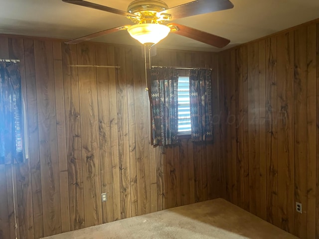 unfurnished room featuring carpet flooring, wood walls, and ceiling fan