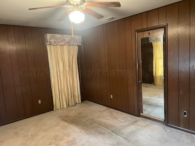 unfurnished bedroom featuring light colored carpet, ceiling fan, and wood walls