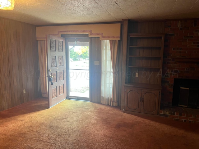 unfurnished living room featuring carpet flooring, wood walls, and a brick fireplace