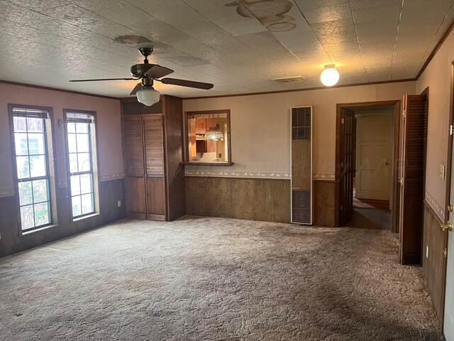 interior space featuring a textured ceiling, carpet floors, ceiling fan, and wood walls