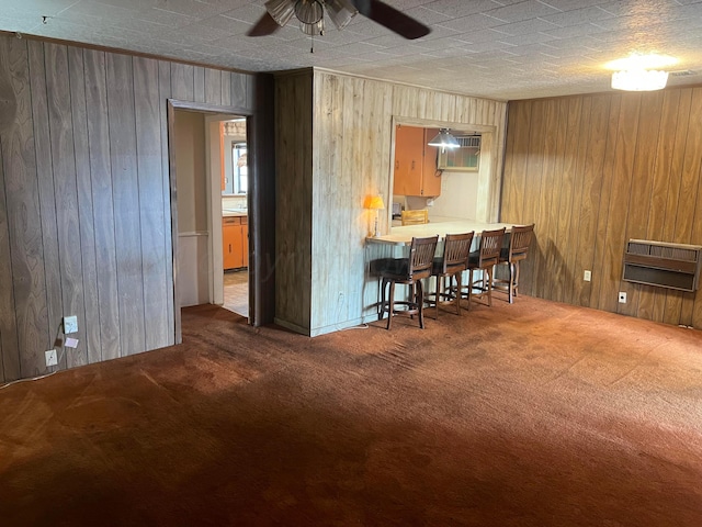 interior space featuring carpet flooring, heating unit, ceiling fan, and wood walls