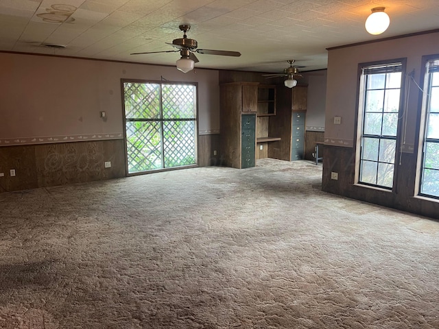 unfurnished living room with carpet, ceiling fan, and wooden walls