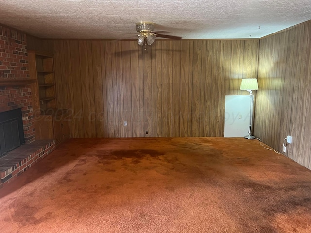 unfurnished living room featuring carpet floors, a textured ceiling, wooden walls, and a brick fireplace