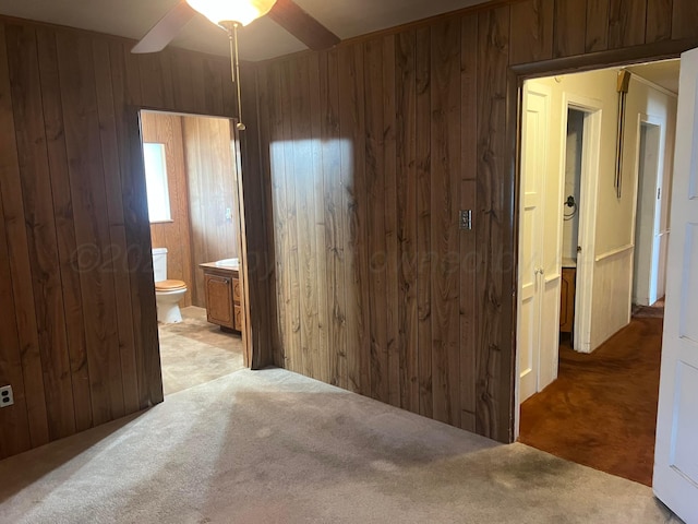 bedroom featuring ceiling fan, wood walls, light carpet, and connected bathroom