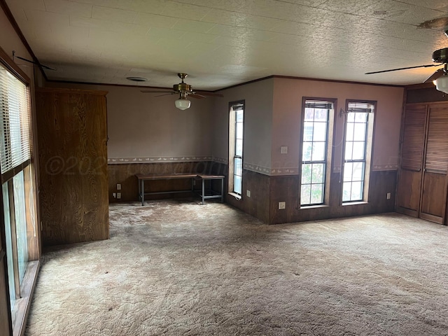 interior space featuring light colored carpet, ceiling fan, and wood walls