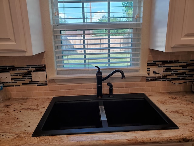 details featuring tasteful backsplash, sink, light stone counters, and white cabinets