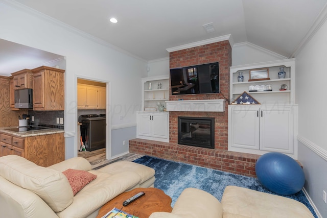 living room with a brick fireplace, washing machine and clothes dryer, crown molding, and vaulted ceiling