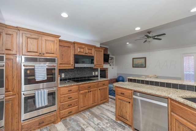 kitchen with vaulted ceiling, ceiling fan, light wood-type flooring, ornamental molding, and appliances with stainless steel finishes