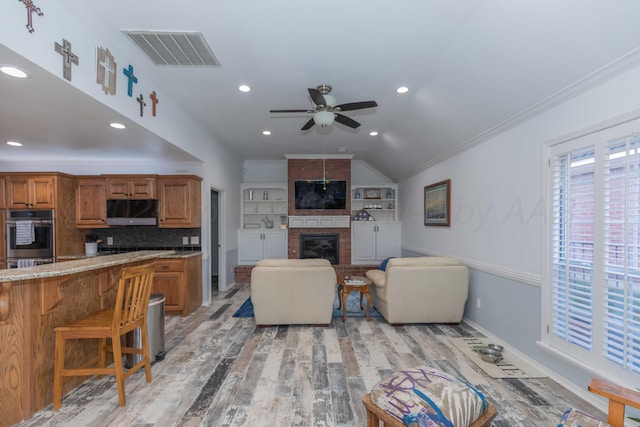 living room with ceiling fan, a brick fireplace, light hardwood / wood-style floors, lofted ceiling, and ornamental molding