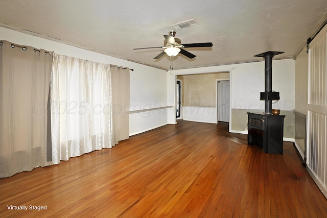 unfurnished living room with a wood stove, hardwood / wood-style floors, and a ceiling fan